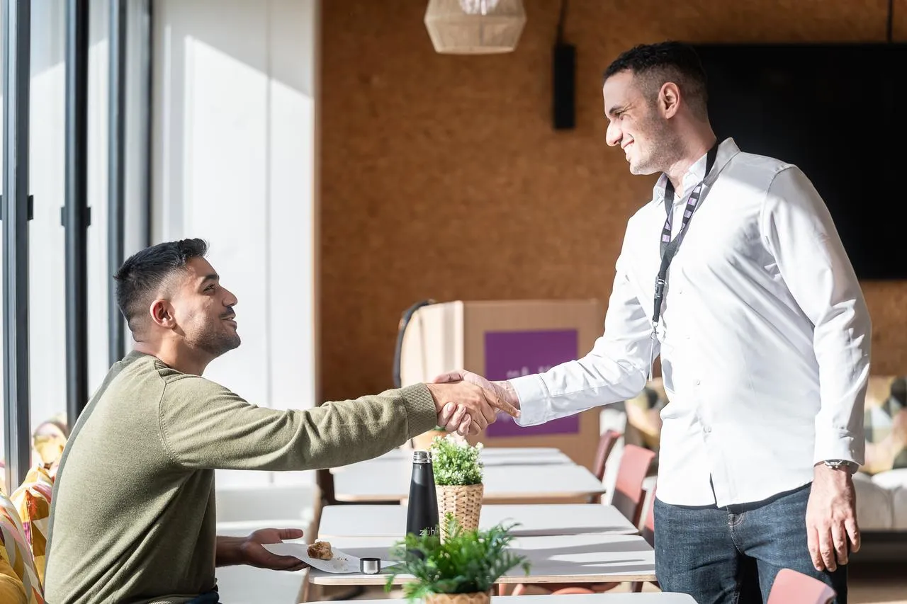 Two men smiling and shaking hands at a lunch table in Zühlke Porto office