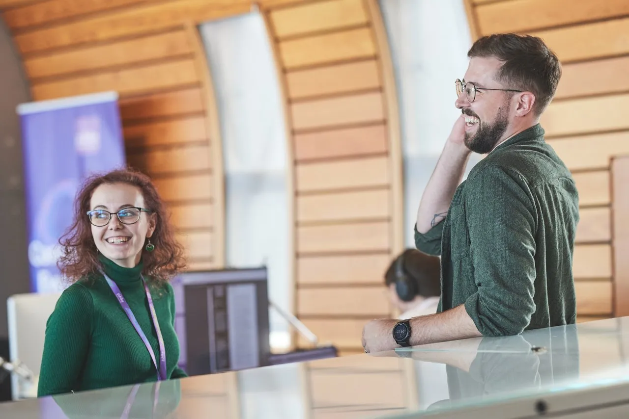 A woman and a man standing opposite each other in an office setting and having a laugh