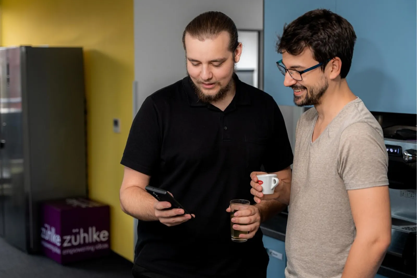 Two men standing in a kitchen looking at a phone