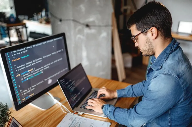 A software engineer uses a Mac and second screen to code