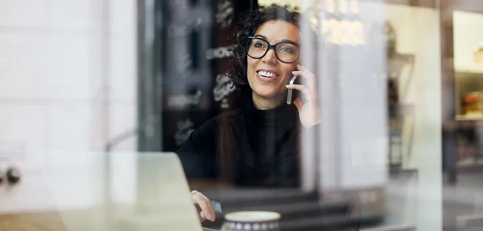 woman on a mobile phone and in front of laptop behind a window