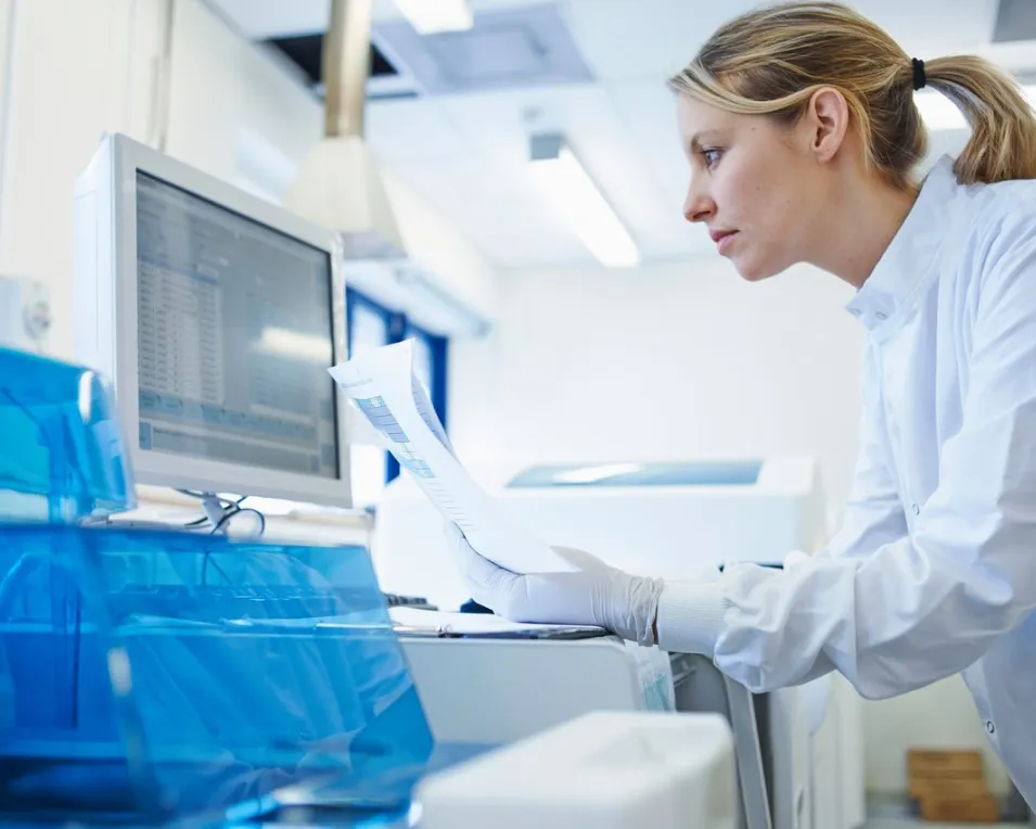 Medical researcher reviewing lab results on screen and printout, reflecting AI-augmented delivery in medical diagnostics software.