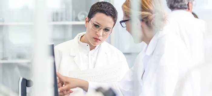 Two women in white medical coats working in a lab at a screen